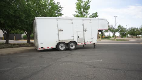 Small-white-gooseneck-cargo-trailer-in-an-empty-parking-lot,-static