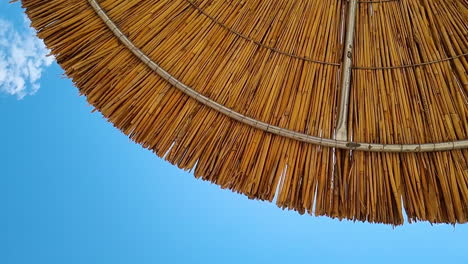 Bottom-up-rotate-view-under-the-reed-straw-beach-umbrella-and-clear-blue-sky-on-a-sunny-day