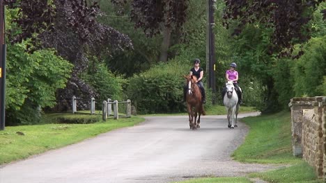Two-female-horse-riders-out-on-a-country-road-gently-exercising-their-horses-on-a-beautiful-afternoon-in-the-English-countryside