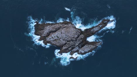 Unique-aerial-view-looking-down-at-a-rocky-outcrop-island-surrounded-by-deep-blue-ocean-waters