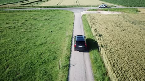 A-large-volvo-xc90-4x4-car-drives-through-the-fields-of-the-Swiss-countryside-and-approaches-an-intersection-with-another-road