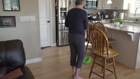 Senior-woman-cleaning-her-hardwood-kitchen-floors---tilt-down