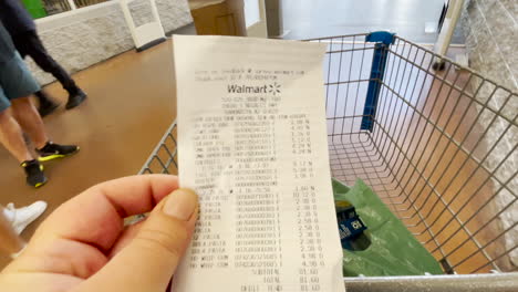 El-Consumidor-Mira-La-Factura-Alta-Del-Supermercado-Después-De-Comprar-En-Walmart-Mientras-Empuja-El-Carrito