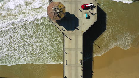 Drone-footage-of-people-walking-on-a-pier,-at-the-ocean,-taken-from-a-drone