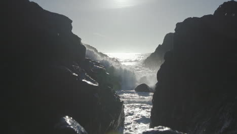 Slow-motion-low-angle-close-up-shot-of-an-ocean-wave-smashing-on-rocks-and-flows-towards-camera