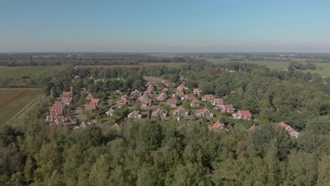 Luftaufnahmen-Nähern-Sich-Einem-Erholungs-Bungalowpark-In-Den-Niederlanden,-Der-In-Einem-Wald-Liegt-Und-Die-Weitere-Umgebung-Und-Den-Horizont-Zeigt