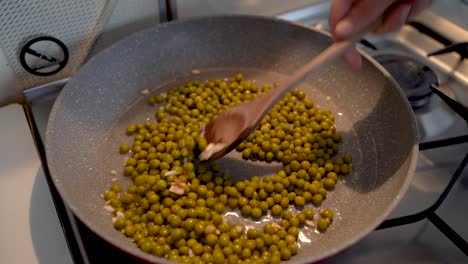 Mixing-Frying-Garlic-And-Peas-With-A-Wooden-Spoon-On-A-Cooking-Pan