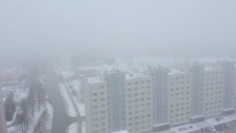 Snowy-and-foggy-close-drone-video-of-a-nine-story-Soviet-style-buildings-with-birds-in-stormy-city