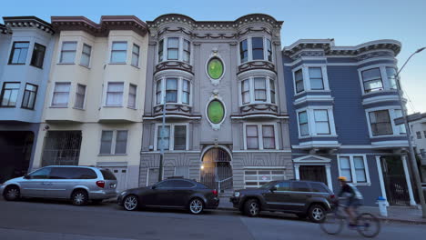 Vorderseite-Des-Viktorianischen-Hauses-Von-San-Francisco-Mit-Seltsamen-Grünen-Fenstern,-Motorroller,-Fahrräder-Und-Autos-Fahren-Vorbei