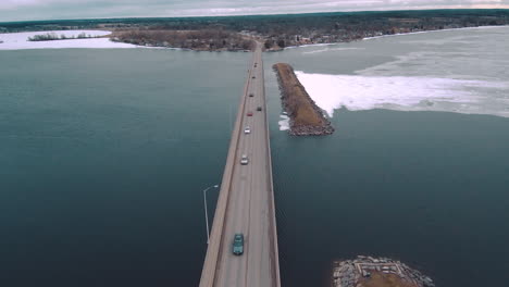 4K-Aerial-Shot-of-Cars-Driving-Over-Icy-Water-on-a-Huge-Highway-Bridge-Surrounded-by-a-Large-Frozen-Lake-Teal-Color-Grade-ProRes