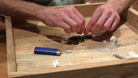 front-view-of-a-man-adding-marijuana-with-tobacco-on-a-wooden-tray-at-the-comfort-of-his-home