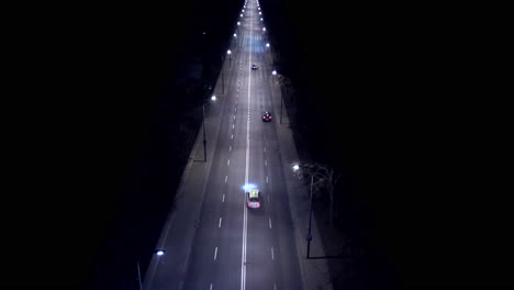 Aerial-view-car-driving-on-City-road-at-dusk-through-dark-surroundings-with-headlights-and-road-lanterns