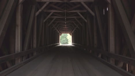 Pushing-in-slowly-through-the-dark,-dramatic-wooden-tunnel-of-the-public-Lowes-covered-bridge-in-Maine
