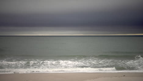 Wellen-Schlagen-Auf-Eine-Küste,-Während-Stimmungsvolle-Wolken-Vorbeiziehen