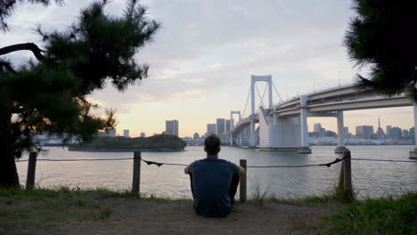 Man-relaxing-by-bridge-to-Tokyo-at-sunset