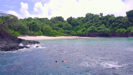 Two-persons-snorkeling-at-the-coast-with-a-sand-beach-and-forest-background