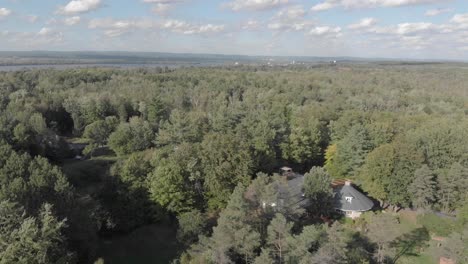 Aerial-footage-over-a-forested-area-with-a-home-surrounded-by-a-lake-and-mountains-on-a-summer-afternoon-in-Ontario-just-outside-of-Ottawa
