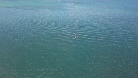 Tilting-drone-shot-of-a-woman-paddling-on-a-SUP-a-distance-from-the-shore