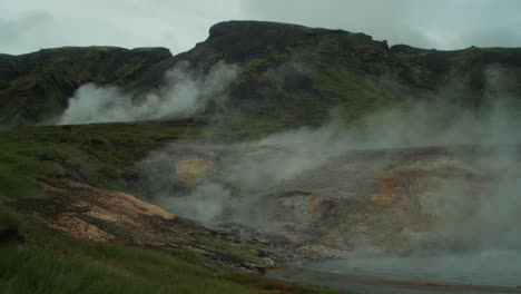 iceland-landscape,-geothermal-hotspring-steam-smoke-rising,-distant-figure-of-photographer-taking-a-picture-of-a-whole-scene,-wide-angle-lens-shot,-camera-pan-from-left-to-right