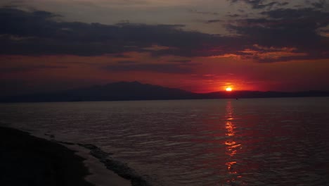 Sunset-time-lapse-on-Thassos-beach,-Greece-with-unidentifiable-people-walking-by-and-a-drone-flying-around