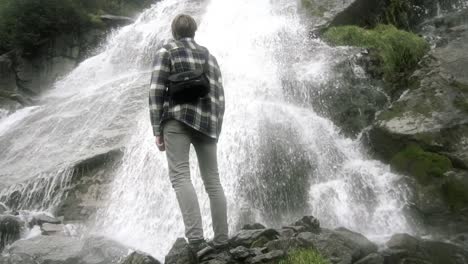 Hombre-Parado-Frente-A-Una-Hermosa-Cascada-En-Noruega,-Europa-Durante-El-Día