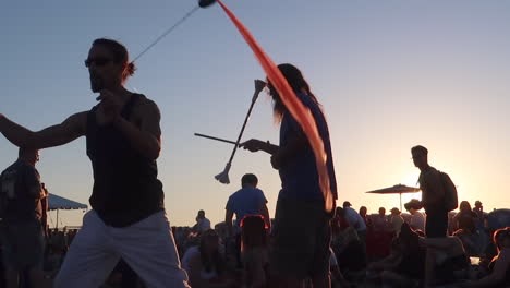 Close-Up-of-a-Man-Performing-with-Poi-Ribbons-at-a-Music-Festival-with-the-Sun-Setting-in-the-Background-in-Slow-Motion