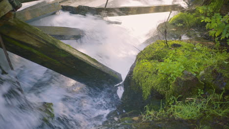 Rushing-Water-Rapids-Crashing-Into-Large-Damaged-Wooden-Beams-with-Moss-Covered-Rocks-4K-ProRes