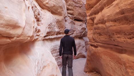 Slow-motion-shot-of-young-man-walking-in-orange-rock-passage-in-Valley-of-Fire-State-Park,-Nevada,-USA