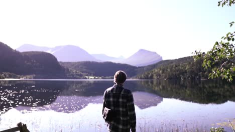 Man-standing-at-a-beautiful-lake,-thinking,-enjoying-and-relaxing-after-a-long-hike,-breathing-in-life,-slow-motion-shot-in-Norway,-Europe