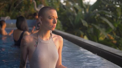 Female-model-contemplatively-looks-toward-the-sun-in-a-tropical-resort-pool