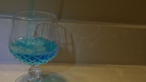 Frontal-shot-of-blue-liquid-being-poured-into-a-wine-glass