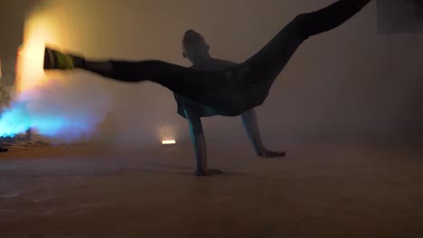 Slow-motion-shot-of-African-youth-doing-break-dancing-spins-on-his-back-in-colorful-blue-smoke