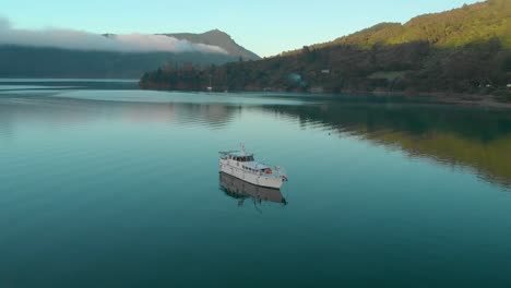 Morning-aerial-flying-around-cruise-boat-anchored-in-bay-in-Marlborough-Sounds,-New-Zealand,-cinematic