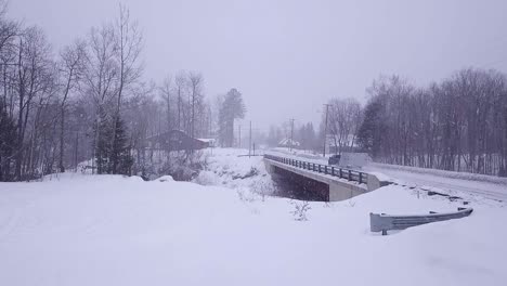 SLOW-MOTION-Aerial-shot-of-truck-towing-snowmobile-trailer-over-a-bridge-during-a-snow-storm