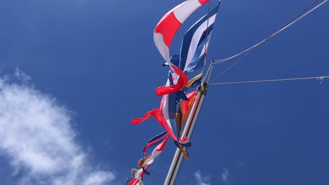 Pan-up-to-variety-of-colorful-flags-blowing-in-strong-breeze-on-boat-mast-with-clouds-and-sky-in-background