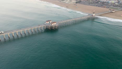 4k-ariel-drone-shot-of-the-pier-in-Huntington-Beach,-Surf-City-USA,-California-as-surfers-catch-waves-and-families-enjoy-summer-vacation