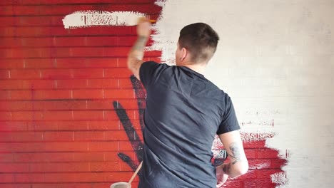 Artista-Tatuado-Pintando-Sobre-Un-Mural-Rojo-En-Una-Pared-De-Ladrillo-Con-Pintura-Blanca