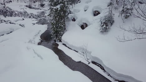 Drone-flying-over-a-creek-in-a-small-snowy-valley-in-the-alps