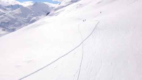 Aerial-establishing-shot-of-people-walking-up-snowy-mountain-in-the-alps