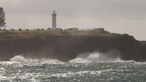 Pull-focus-through-rain-of-waves-breaking-onto-the-rocks-at-the-foot-of-a-lighthouse