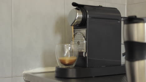 Espresso-coffee-made-from-a-machine-into-a-transparent-glass-cup-before-being-picked-up-by-a-man-wearing-a-white-shirt