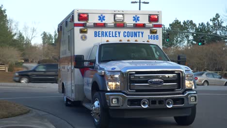 Ambulance-sits-at-busy-intersection-with-traffic-in-background-and-emergency-lights-flashing