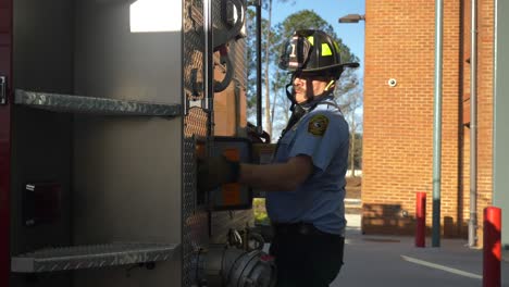 Firefighter-works-around-gear-and-fire-hoses-on-a-fire-truck-early-in-the-morning-to-prep-for-emergency-response