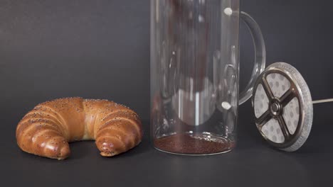 CLOSEUP---Filling-french-press-with-ground-coffee-next-to-a-breakfast-croissant