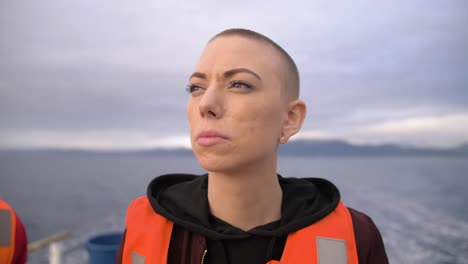 Slow-motion,-close-up-view-of-woman-with-shaved-head-wearing-a-life-preserver-while-on-a-boat-in-motion
