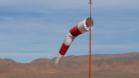 Close-up-of-an-isolated-windsock-blowing-gently-in-the-wind-at-a-desert-airfield,-high-mountains-in-the-background