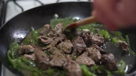 closeup-uncovering-smoking-pan-with-meat-and-green-pepper,-stiring-with-wooden-spoon