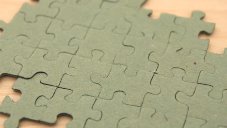 Close-up-of-a-young-girl's-hand-putting-a-puzzle-piece-in-the-last-blank-spot-concluding-a-single-color-puzzle,-on-a-light-wooden-background