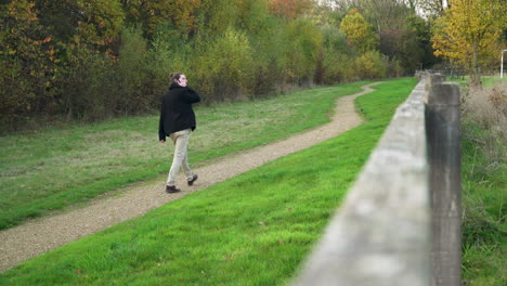 Man-on-phone-call-walks-down-dirt-path-in-a-park-away-from-camera