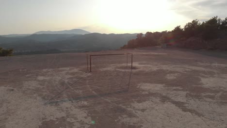 Aerial:-Empty-football-or-soccer-goal-on-hard-ground-pitch-at-sunset